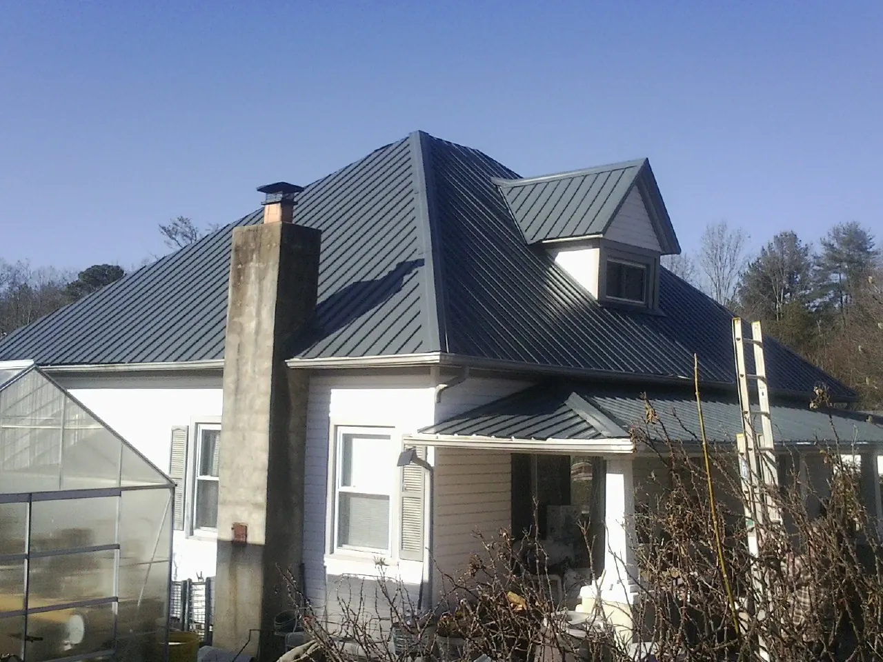 Dark blue standing seam metal roof on a white farmhouse with dormer — Slate & Tile Roof Repair by Roofing Brothers in Silver Plume