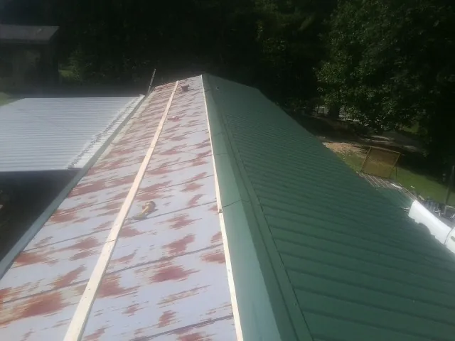 Old rusted panels beside newly installed green metal roofing — Wind Damage Roof Repair by Roofing Brothers in Silver Plume
