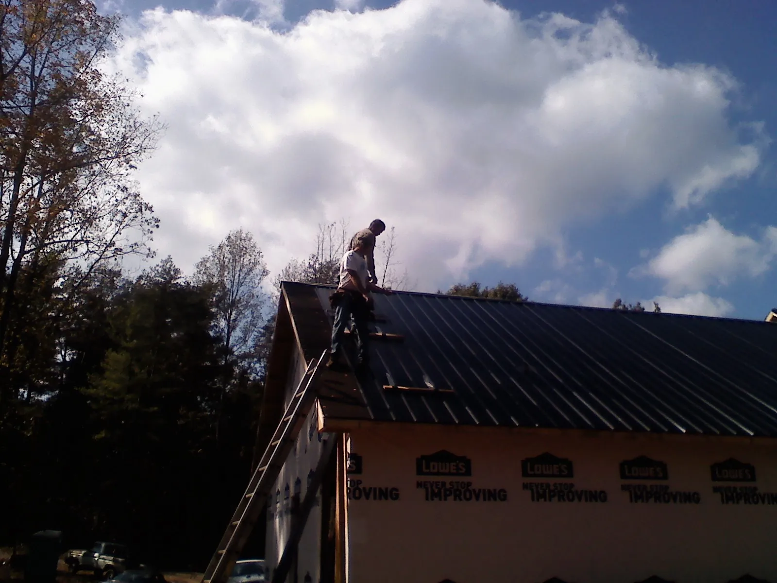 Roofer fastening dark metal panels high against a cloudy sky, from a Roof Inspection job in Silver Plume