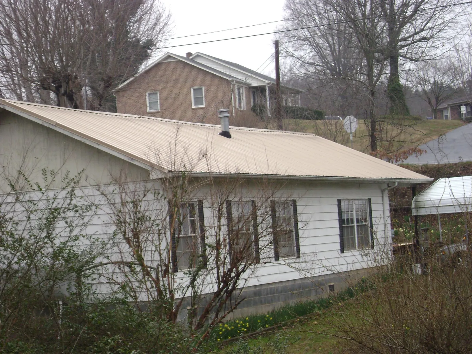 Tan metal roof on a white sided house set into a hillside — Commercial Roofing by Roofing Brothers in Silver Plume